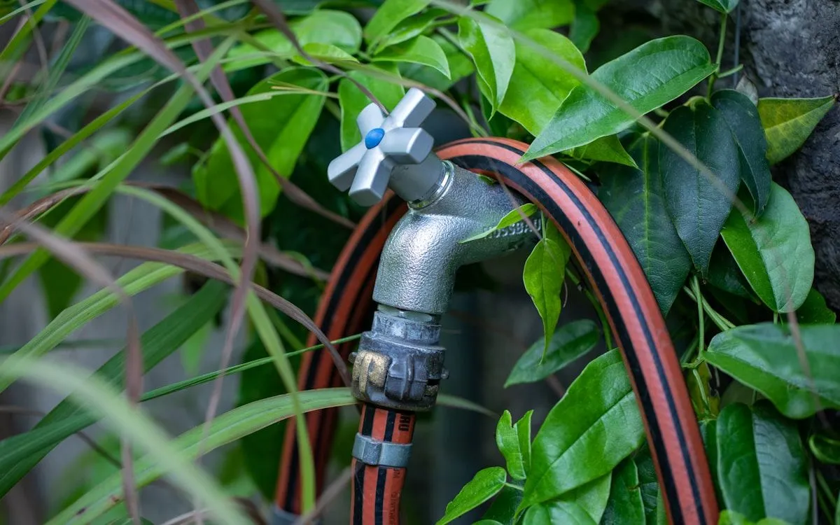 Jardinier purgeant un tuyau d'arrosage avec un compresseur à air avant l'hiver.
