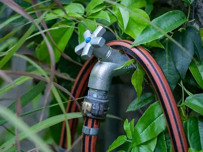 Jardinier purgeant un tuyau d'arrosage avec un compresseur à air avant l'hiver.